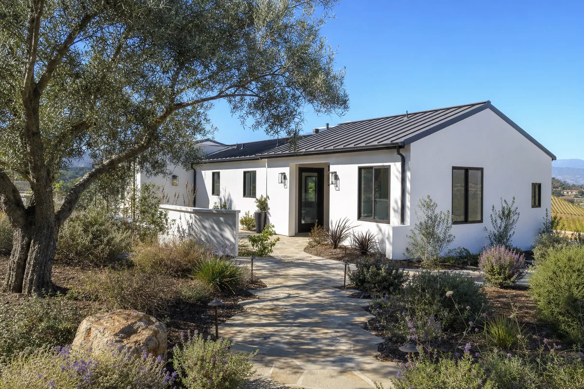 Modern farmhouse style ADU at twilight in a Temecula backyard with white board-and-batten siding, dark metal roof, glowing interior lights, and a covered porch.
